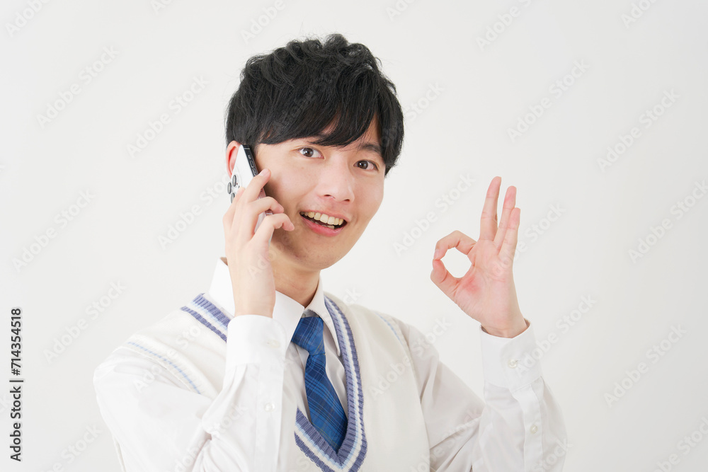 スマートフォンで電話しながらOKサインをする男子高校生 白背景 スマートフォンで電話しながらOKサインをする男子高校生 白背景