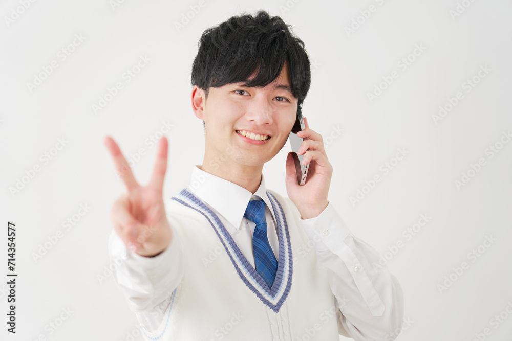 スマートフォンで電話しながらピースサインをする男子高校生 白背景 スマートフォンで電話しながらピースサインをする男子高校生 白背景