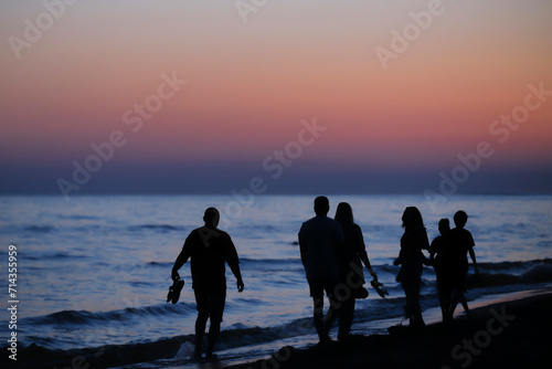 A group of people walking on the beach in sunset. Silhouettes of the people on the sea coast in evening time.