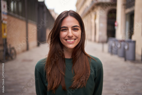 Close up portrait joyful beautiful young Caucasian gen z woman happy smiling on city street. Female people with nice expression looking at camera in open air. Spanish girl posing for picture outdoor