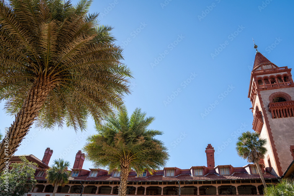 Tall palm trees in the foreground with historic red-tiled building under clear blue sky.