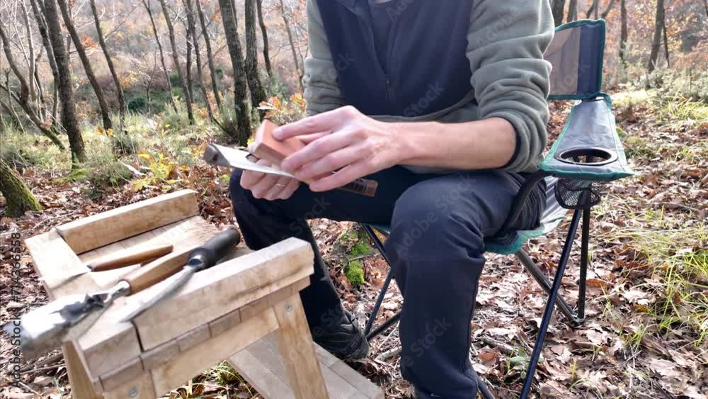 Man prepares an axe by using sharpener before wood carving. Carving equipments on the stand.