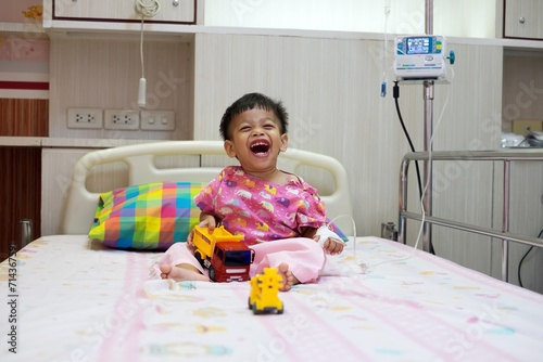 2-year-old baby in patient uniform Lying laughing, smiling in a hospital bed.