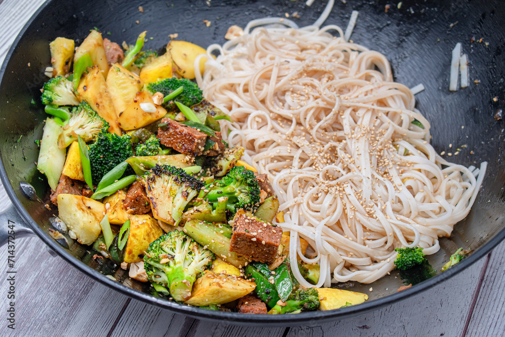 Vegan broccoli, seitan and squash stir fry in wok, along with rice noodles StockFoto Adobe Stock
