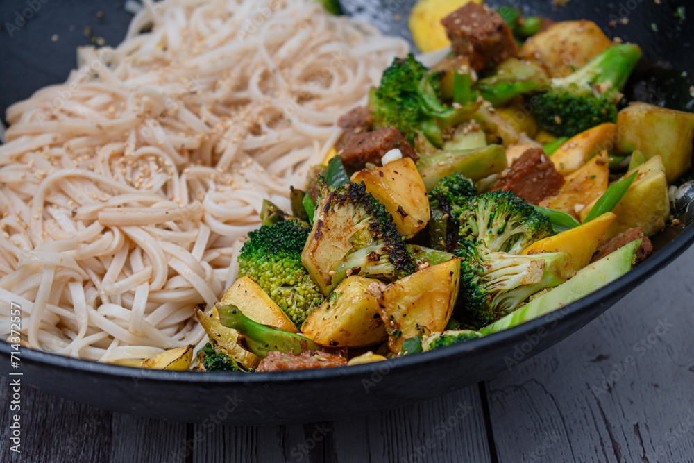 Vegan broccoli, seitan and squash stir fry in wok, along with rice noodles Photos Adobe Stock