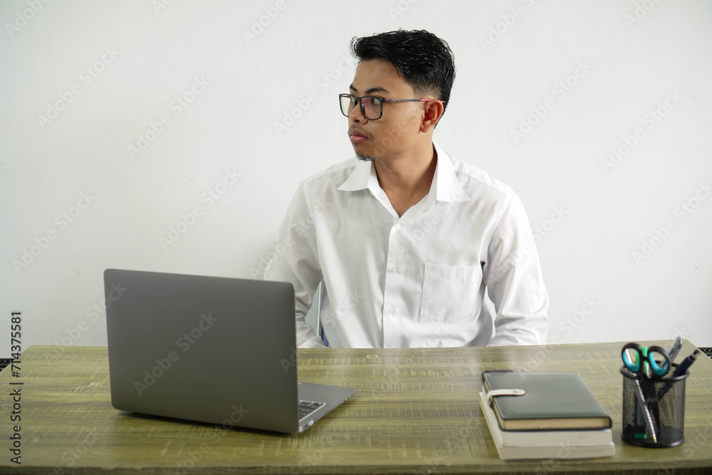 young asian businessman in a workplace making doubts gesture looking side, wearing white shirt with glasses isolated young asian businessman in a workplace making doubts gesture looking side, wearing white shirt with glasses isolated