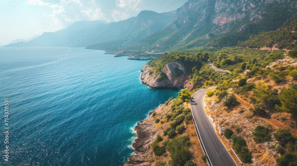 an aerial view of a road on the side of a mountain with a body of water in the foreground and a cliff on the other side of the road. an aerial view of a road on the side of a mountain with a body of water in the foreground and a cliff on the other side of the road.