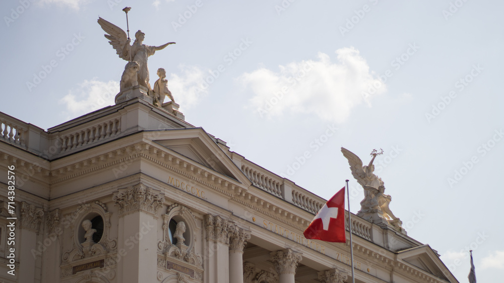 Obraz premium Majestic Statues Adorning the Rooftop of an Elegant European Building With Swiss Flag