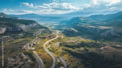  an aerial view of a winding road in the mountains with a view of a valley and mountains in the distance with a blue sky and white cloud filled with wispe.