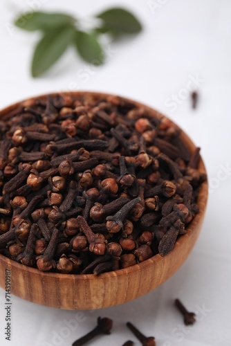 Aromatic cloves in bowl on white tiled table, closeup