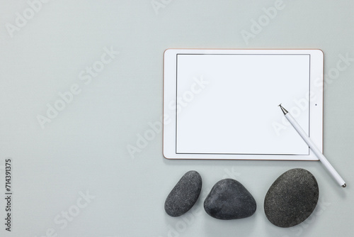 Modern tablet, stylus and pebbles on light grey background, flat lay. Space for text