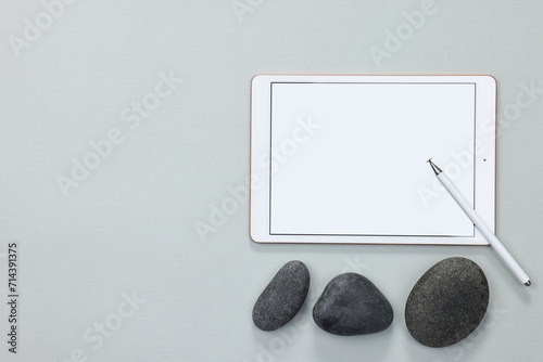 Modern tablet, stylus and pebbles on light grey background, flat lay. Space for text photo