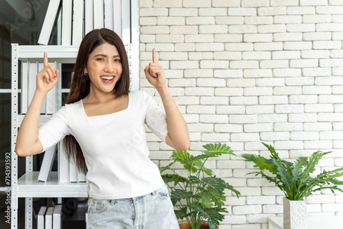 Young woman standing posing confident looking at camera and smiling with Point index finger overhead