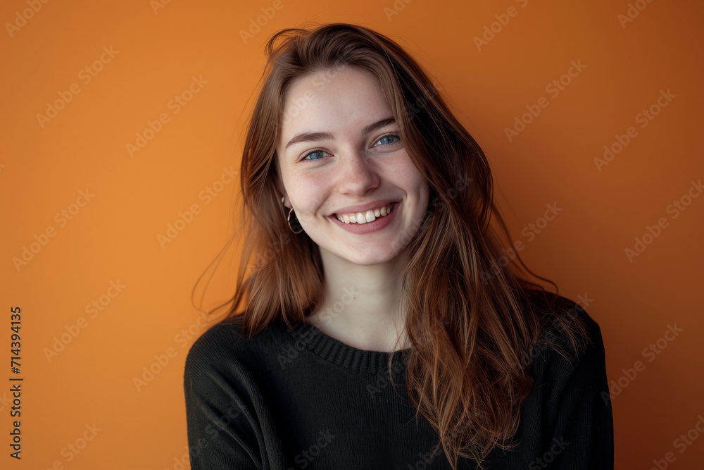 A woman in a black sweater smiles in front of an orange wall A woman in a black sweater smiles in front of an orange wall