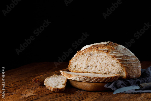 Rustic sourdough bread with cut slices on a wooden table. Panorama, black background with free space for text.