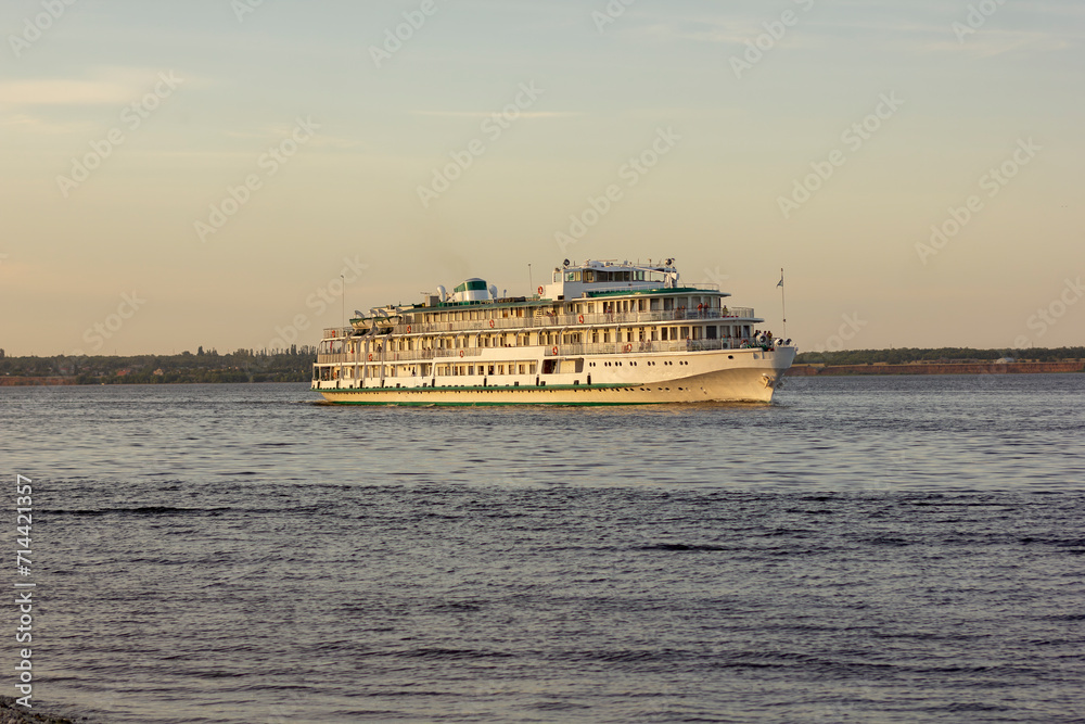 a large white motor ship cruises along the river in summer