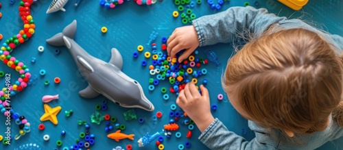 Child developing creativity and fine motor skills by crafting a dolphin from beads. Overhead perspective.