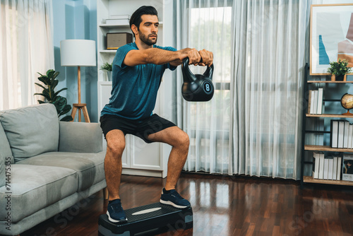 Athletic body and active sporty man doing squat with kettlebell weight for effective targeting muscle gain at gaiety home as concept of healthy fit body home workout lifestyle. photo