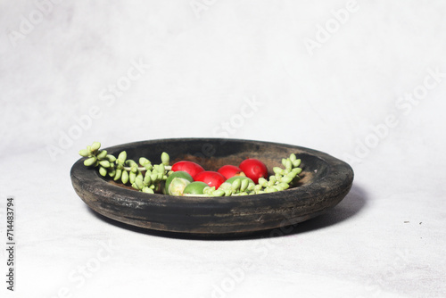 Green and red palm fruits (buah palem) on wooden plate.