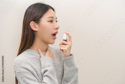Health care treatment sore throat concept, sick pain asian young woman have cough symptom holding medicine bottle, using spray in mouth to protect disease from bacteria, illness from virus infection. photo
