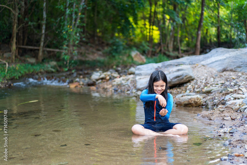 Fototapeta Naklejka Na Ścianę i Meble -  Asian child or kid girl sitting smiling playing in nature water stream and garden forest at phalad waterfall in lan sang national park at Tak Thailand for summer holiday relax and travel to happy fun