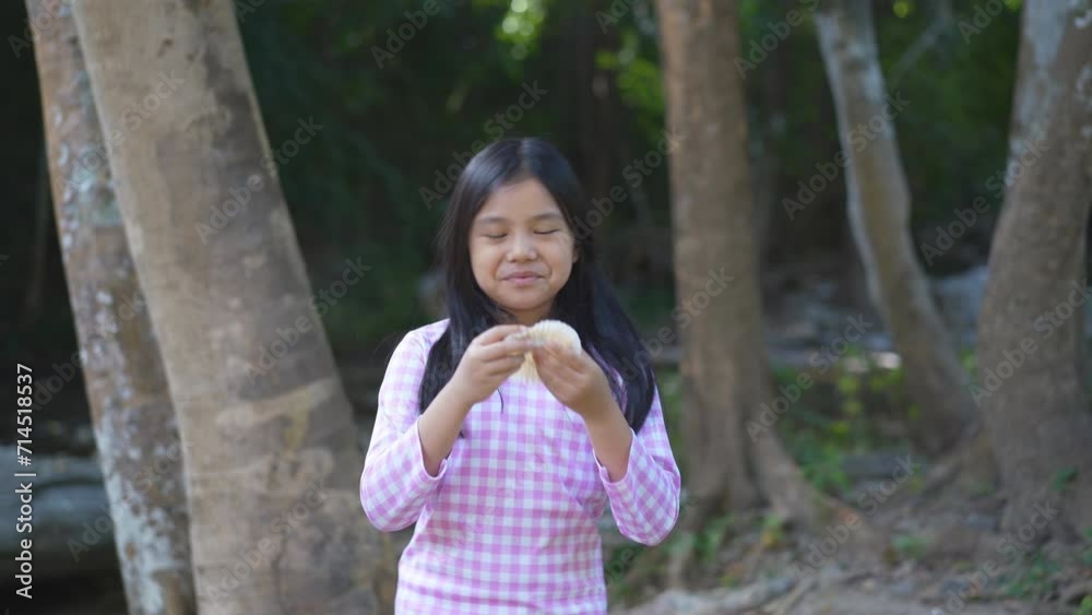 asian child or kid girl standing enjoy eating delicious snack banana cake and happy smile to cheerful in garden nature with stream on holiday travel or young people hungry to eat bread dessert 4K asian child or kid girl standing enjoy eating delicious snack banana cake and happy smile to cheerful in garden nature with stream on holiday travel or young people hungry to eat bread dessert 4K