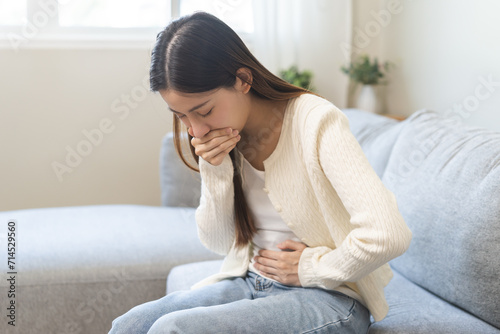 Unhappy pregnant asian young woman, pain girl suffering from nausea, having vomit feeling sick covering mouth, touching belly having problem throwing up from food poisoning, lady with morning sickness photo