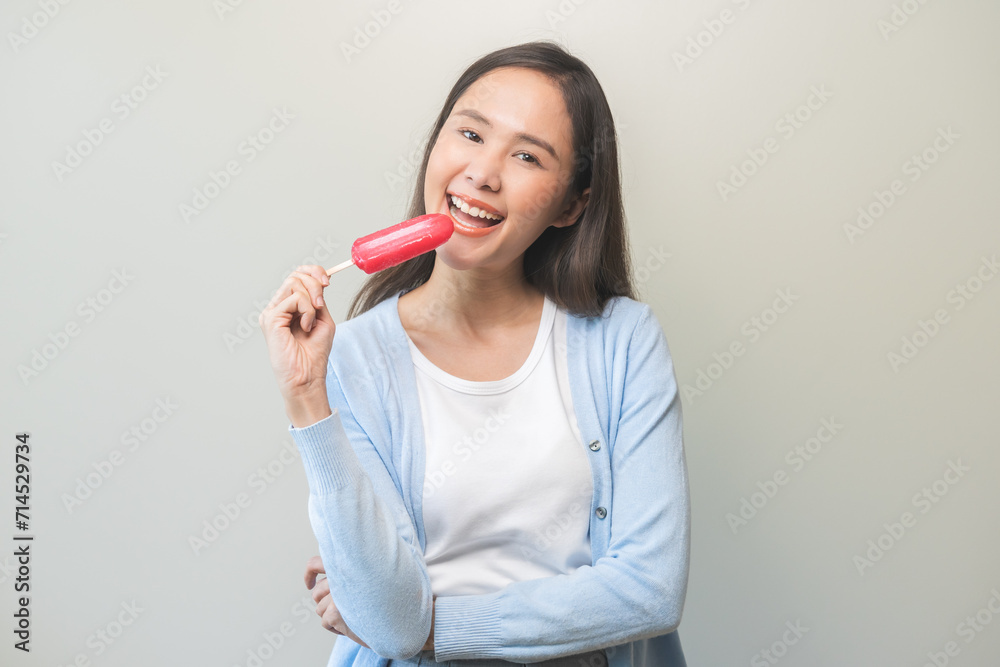 Cheerful, happy positive asian woman wearing casual with brunette hair, enjoy eating delicious popsicle, girl holding cold dessert, frozen stick with strawberry ice cream tasty isolated on background. Cheerful, happy positive asian woman wearing casual with brunette hair, enjoy eating delicious popsicle, girl holding cold dessert, frozen stick with strawberry ice cream tasty isolated on background.