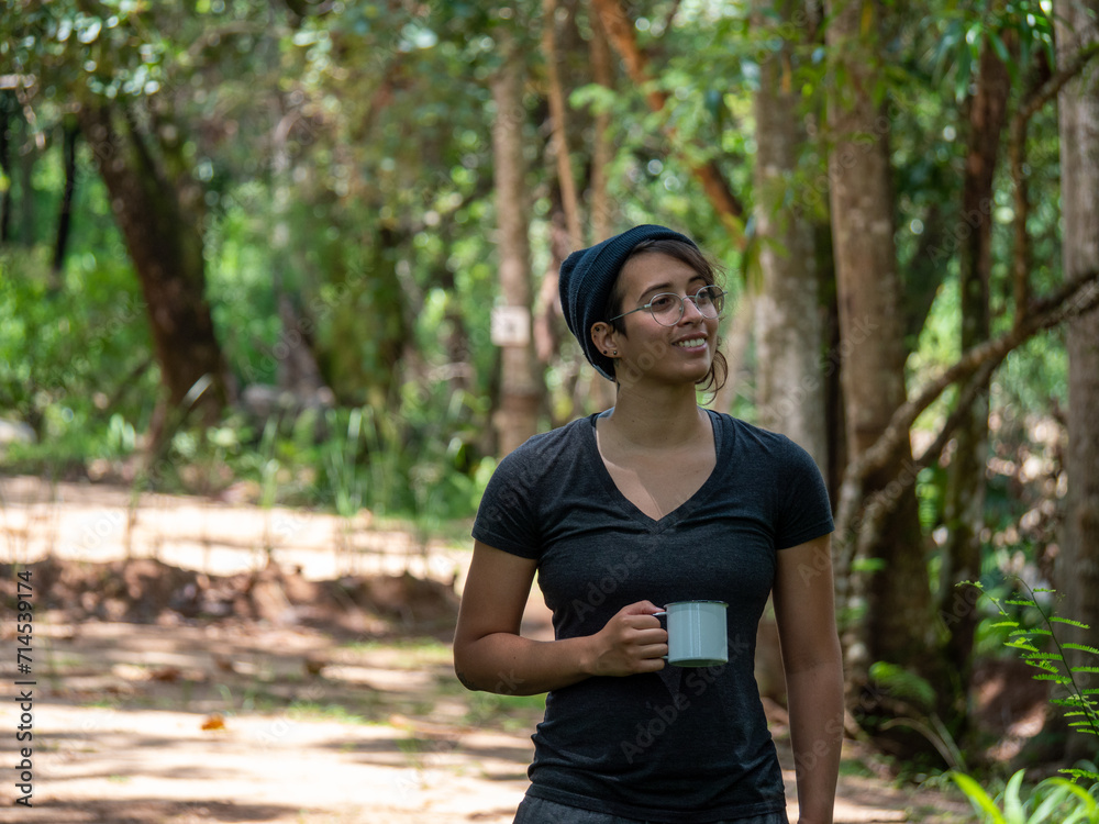 Étudiante dans la nature avec un style décontracté buvant dans une tasse métallique de camping. Concept de voyage Étudiante dans la nature avec un style décontracté buvant dans une tasse métallique de camping. Concept de voyage