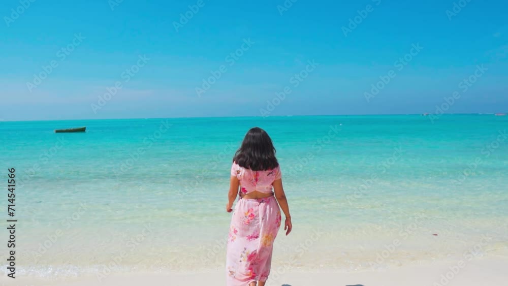 Slow motion shot of Indian woman wearing beautiful pink dress walking by beach at Lakshadweep Island, India. Female tourist on summer vacation. Beautiful white sand beach with turquoise color water. Slow motion shot of Indian woman wearing beautiful pink dress walking by beach at Lakshadweep Island, India. Female tourist on summer vacation. Beautiful white sand beach with turquoise color water.