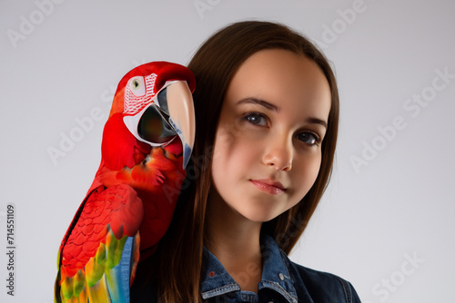 girl with a parrot. a young beautiful girl with long hair and a denim jacket stands on a gray background with a bright large parrot on her shoulder