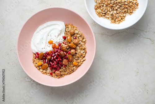 Granola bowls with yogurt, pomegranate seeds and nuts, top view on a light-beige stone background, horizontal shot with space