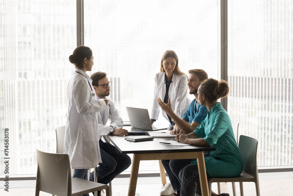Young clinic chief man talking to diverse staff of doctors at meeting table, giving consultation of expert to listening multiethnic practitioners. Medical colleagues discussing job, treatment case Young clinic chief man talking to diverse staff of doctors at meeting table, giving consultation of expert to listening multiethnic practitioners. Medical colleagues discussing job, treatment case