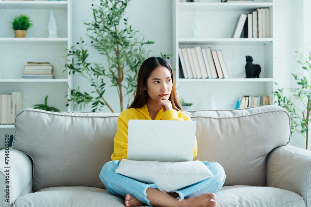 Happy young Asian woman using laptop while seated on couch at home Happy young Asian woman using laptop while seated on couch at home