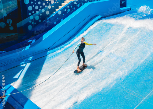Beautiful young woman surfing on a wave simulator at a water amusement park