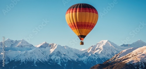  a hot air balloon flying in the sky over a mountain range with a snow covered mountain range in the distance in the distance is a blue sky with a few clouds.