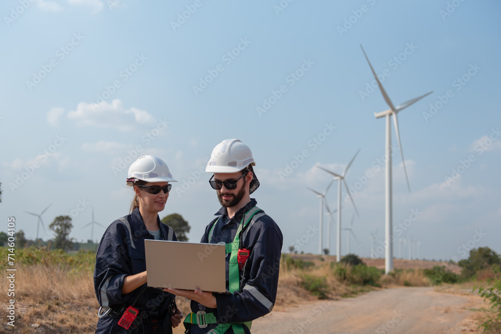 Engineers working and using a computer laptop on site in wind turbine farm, Wind turbines generate clean energy source, Eco technology for electric, industry environment Engineers working and using a computer laptop on site in wind turbine farm, Wind turbines generate clean energy source, Eco technology for electric, industry environment