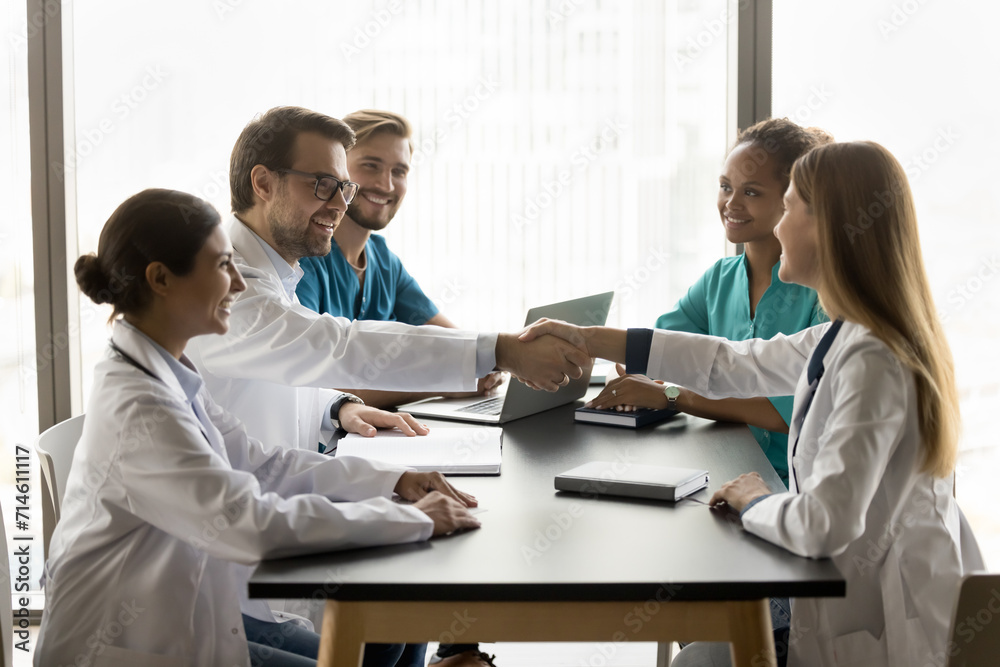 Cheerful young male doctor shaking hands with colleagues woman on medical seminar, cooperation meeting, smiling, laughing, getting agreement with handshake. Diverse clinic staff discussing healthcare Cheerful young male doctor shaking hands with colleagues woman on medical seminar, cooperation meeting, smiling, laughing, getting agreement with handshake. Diverse clinic staff discussing healthcare