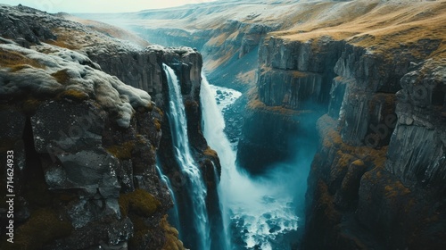  an aerial view of a waterfall in the middle of a rocky area with snow on the ground and grass growing on the sides of the sides of the cliffs.