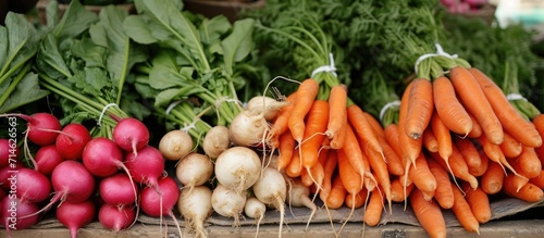 Fresh vegetables, including carrots, radishes, and leaks, arranged attractively at a flea market stall.