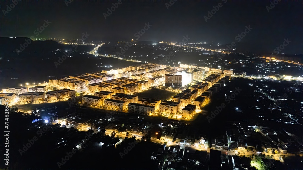 Fototapeta premium Aerial night view of a densely populated urban area illuminated with streetlights, showcasing the grid layout of streets and buildings