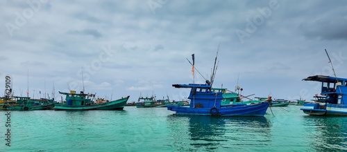 Traditional wooden fishing boats with colorful flags anchored in a calm turquoise sea with an overcast sky photo