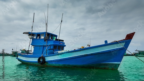 Blue fishing boat floating on calm sea with cloudy sky in the background, depicting maritime or fishing industry concept