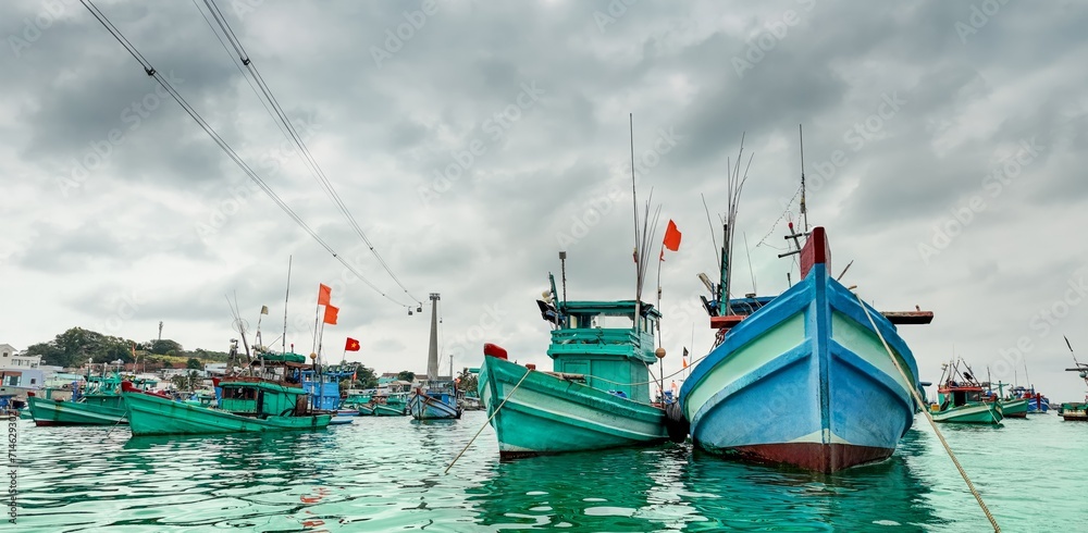 Traditional wooden fishing boats docked at a Southeast Asian fishing village under an overcast sky