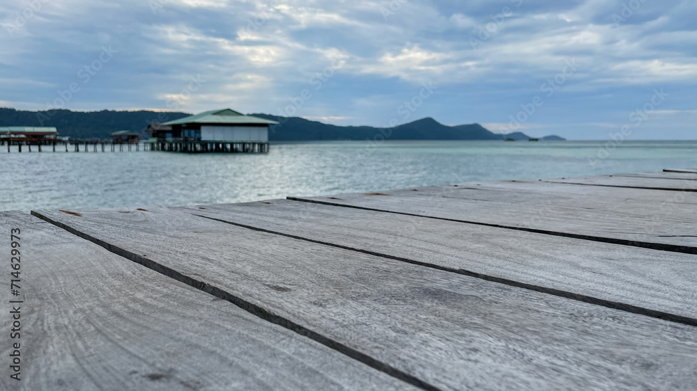 Wooden pier leading to overwater bungalows with calm sea and mountains in the background, evoking a tranquil tropical getaway concept