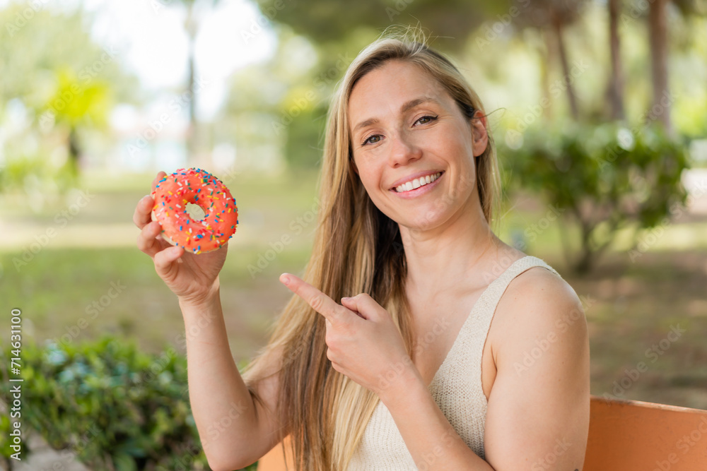 Young blonde woman holding a donut at outdoors and pointing it Young blonde woman holding a donut at outdoors and pointing it