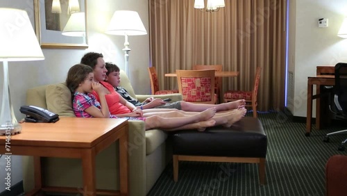 Barefoot woman with two children sit on couch and watch tv in room photo