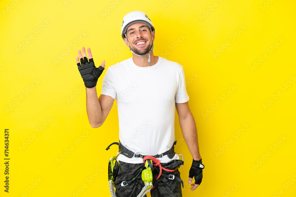 Young rock- climber man isolated on yellow background saluting with hand with happy expression
