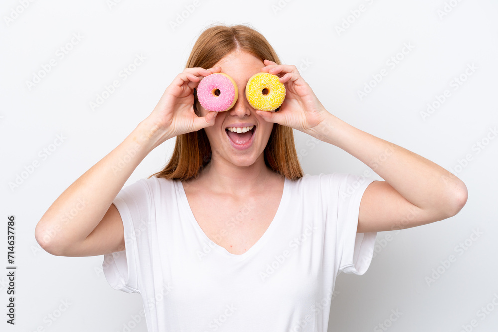 Young redhead woman isolated on white background holding donuts in an eye Young redhead woman isolated on white background holding donuts in an eye