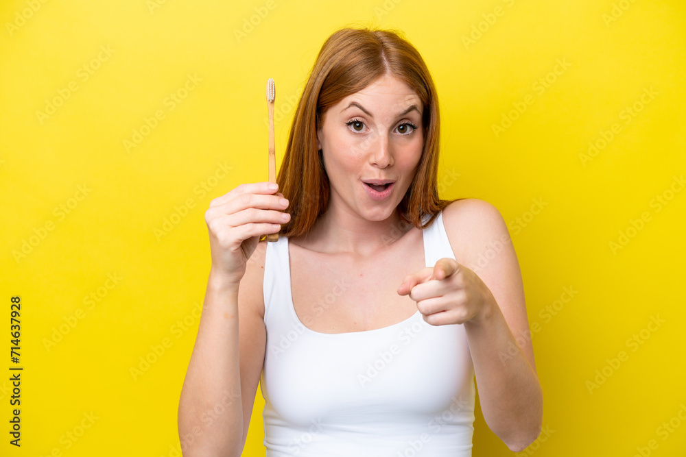 Young redhead woman brushing teeth surprised and pointing front Young redhead woman brushing teeth surprised and pointing front